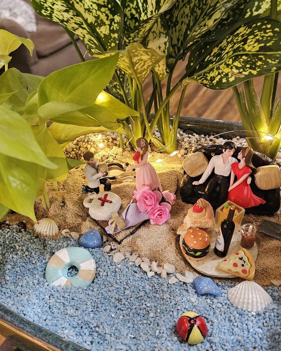 A shoreline built in miniature with sand, shells and small figures among the planting.